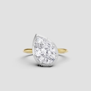 May include: A pear-shaped diamond ring with a gold band and a platinum bezel setting. The diamond is the focal point, showcasing its brilliance. The ring is set against a neutral background, highlighting its elegant design.