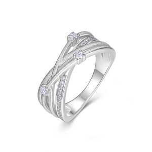 Puede incluir: Un anillo plateado con un dise&ntilde;o fluido e entrelazado. El anillo presenta tres piedras claras m&aacute;s grandes y una fila de piedras m&aacute;s peque&ntilde;as. La banda tiene una apariencia texturizada y cepillada, creando un aspecto moderno y elegante. El anillo est&aacute; sobre un fondo blanco.
