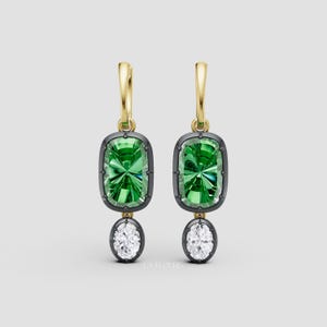 May include: A pair of gold-tone hoop earrings with a rectangular green gemstone and a white oval gemstone. The green gemstone is set in a dark gray frame. The earrings are displayed against a light gray background.