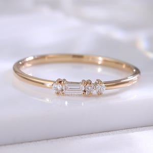 Op de afbeelding: Een delicate gouden ring met een slanke band. De ring heeft een centrale baguette-geslepen diamant, geflankeerd door twee ronde diamanten aan weerszijden. De diamanten schitteren tegen het gepolijste goud.