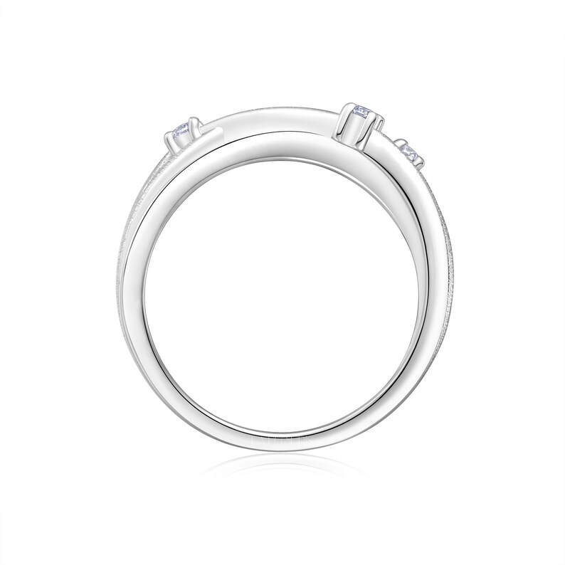 Puede incluir: Un anillo plateado con un dise&ntilde;o &uacute;nico, adornado con peque&ntilde;as piedras preciosas transparentes. El anillo presenta una ca&ntilde;a dividida y una superficie texturizada, creando un aspecto moderno y elegante. Las piedras preciosas est&aacute;n engastadas para a&ntilde;adir brillo.