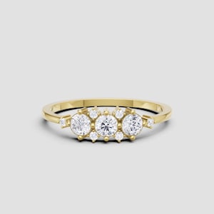 May include: A gold ring with three large, round, clear gemstones in the center, flanked by smaller gemstones. The ring has a delicate band and is set against a light gray background. A piece of jewelry.