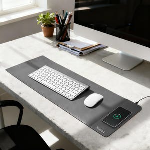 K&ouml;nnte beinhalten: Eine graue Schreibtischunterlage mit kabellosem Ladepad, Tastatur und Maus. Ein Smartphone wird auf dem Pad geladen. Auf der Matte steht der Name "Nolan". Ein Blumentopf, Bleistifte und ein Computer befinden sich ebenfalls auf dem Schreibtisch.