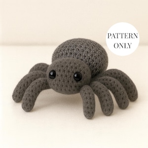 May include: A crocheted spider in shades of gray, featuring a textured body and eight curved legs. The spider has large, black, round eyes. The text "PATTERN ONLY" is in a white circle in the upper right corner.