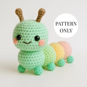 May include: A crocheted caterpillar toy in shades of green, yellow, and pink. The caterpillar has a smiling face with black eyes and pink cheeks. The text "PATTERN ONLY" is in a white circle.