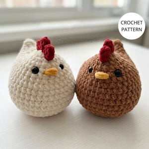 Può includere: Due polli all'uncinetto rotondi e morbidi, uno color crema e uno marrone, ciascuno con una cresta rossa, un piccolo becco giallo e occhi a perla neri. Il testo CROCHET PATTERN è visibile in un cerchio bianco nell'angolo in alto a destra.