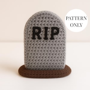 Puede incluir: Una lápida gris tejida a ganchillo con las letras "RIP" en negro. La lápida está colocada sobre una base marrón. Un círculo blanco con las palabras "PATTERN ONLY" está en el fondo.