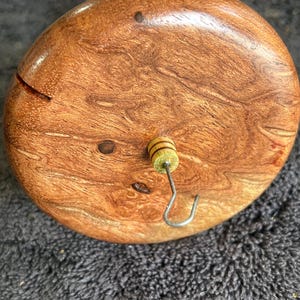 May include: A wooden drop spindle with a round, polished, brown whorl. The whorl has a small metal hook and a decorative, striped bead. The spindle is used for hand spinning yarn and fiber.