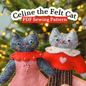 Op de afbeelding: Twee handgemaakte vilten kattenornamenten. Eén kat draagt een roze jurk met een zuurstokontwerp, de andere een rode trui en een bruine broek. De tekst "Celine the Felt Cat PDF Sewing Pattern" staat bovenaan.