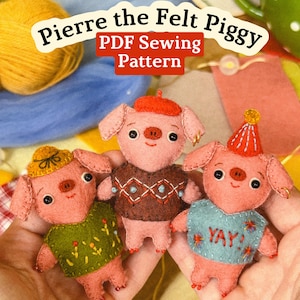May include: Three small pink felt pig dolls featuring embroidered details. The left pig wears a yellow hat and green sweater, the center pig wears a red beret and brown sweater, and the right pig wears a party hat and blue sweater with YAY! text.