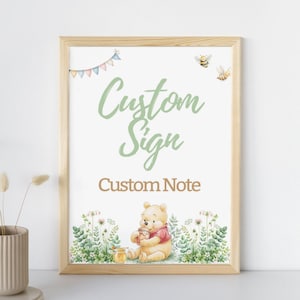 May include: A framed print with the words "Custom Sign" and "Custom Note" in green and brown script. The image features a watercolor illustration of Winnie the Pooh, bees, and floral elements. The frame is made of light-colored wood.