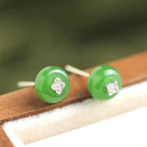 May include: A pair of green jade earrings with a small diamond accent in the center of each earring.