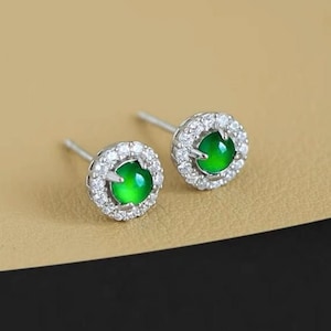 May include: A pair of silver earrings with a green gemstone surrounded by a halo of small clear stones.
