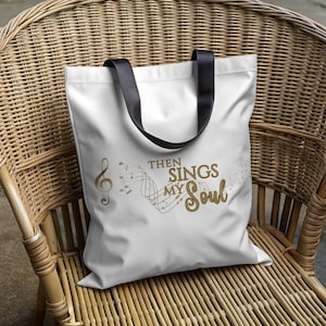 Puede incluir: Bolsa de tela blanca con asas negras que presenta un diseño de nota musical dorada y el texto "Then Sings My Soul".