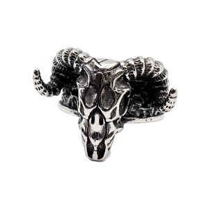 Może przedstawiać: Srebrny pierścionek z detalicznym wzorem czaszki barana. Pierścionek jest wykonany z metalu i ma fakturowane wykończenie.