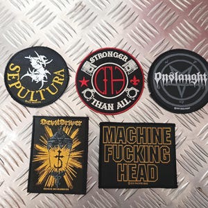 May include: A selection of black and yellow embroidered patches, each displaying band logos and text. The patches feature the band names "Sepultura", "Onslaught", "DevilDriver", and "Machine Fucking Head". The "Stronger Than All" patch is also visible.