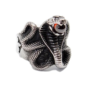 Op de afbeelding: Een zilveren ring met een gedetailleerd cobra-ontwerp. De ogen van de cobra zijn rood.
