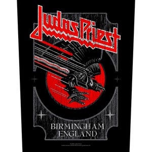 Könnte beinhalten: Schwarze Grafik mit dem roten Bandnamen "Judas Priest" über einem stilisierten Adlerdesign mit roten Akzenten. Der Text "BIRMINGHAM ENGLAND" befindet sich darunter, vor einem strukturierten grauen Hintergrund.