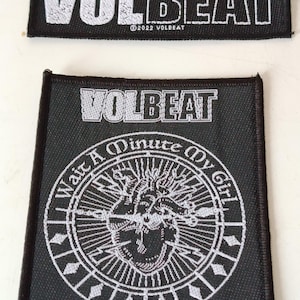 Puede incluir: Dos parches bordados en blanco y negro. El parche superior dice "VOLBEAT" en letras blancas. El parche inferior presenta el nombre de la banda, un diseño de corazón y el texto "Wait A Minute My Girl". Ambos parches tienen el año de copyright.