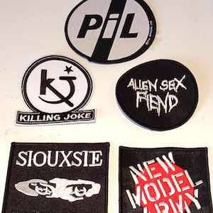Op de afbeelding: Een verzameling zwart-witte geborduurde patches met bandlogo's en tekst. De patches bevatten "P.I.L", "Killing Joke", "Alien Sex Fiend", "Siouxsie and the Banshees" en "New Model Army".