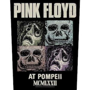May include: Black poster featuring the words "PINK FLOYD" in a distressed font. Below the text are four mosaic-style skull images in various colors. The text "AT POMPEII MCMLXXII" is at the bottom.