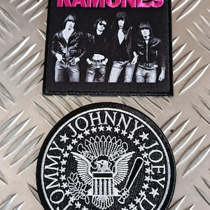 Può includere: Due toppe ricamate. La toppa superiore è quadrata, nera e presenta la scritta "RAMONES" in rosa, sopra un'immagine in bianco e nero della band. La toppa inferiore è rotonda, in bianco e nero, con un'aquila, stelle e i nomi "TOMMY", "JOHNNY" e "JOEY" sul bordo.