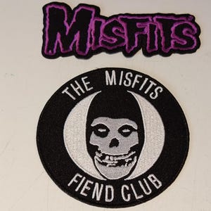 May include: Two embroidered patches. The top patch reads "Misfits" in purple lettering with a black outline. The bottom patch is circular, black with white text that reads "The Misfits Fiend Club". The center of the patch features a white skull.