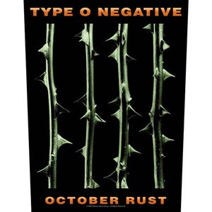 Pode incluir: Fundo preto com quatro caules verticais com espinhos afiados. O texto "TYPE O NEGATIVE" está no topo e "OCTOBER RUST" na parte inferior, em letras laranja. A imagem é um gráfico promocional.