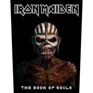 Könnte beinhalten: Ein schwarzer, rechteckiger Stoffaufnäher mit dem weißen Iron Maiden-Logo oben und dem Schriftzug The Book of Souls unten. In der Mitte befindet sich eine detaillierte Abbildung einer Kreatur mit roten Augen und einem strukturierten braunen Gesicht.