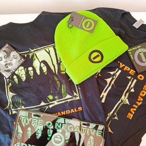 Op de afbeelding: Een fel neon-groene gebreide muts met een ronde logopatch, twee zwarte t-shirts met Type O Negative bandafbeeldingen en tekst, en een rechthoekig kentekenplaathouder met de tekst Type O Negative en 4DXFRMBRKLYN.