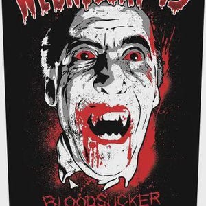 May include: A black graphic print featuring the text WEDNESDAY 13 at the top and BLOODSUCKER MOTHERFUCKER at the bottom. The central image is a high-contrast, stylised portrait of a vampire with red eyes, sharp fangs, and blood dripping.