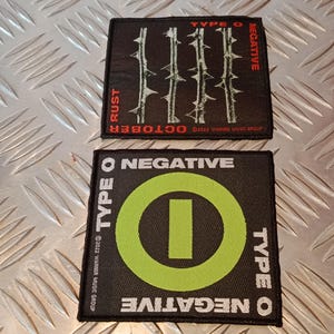 Pode incluir: Duas aplicações quadradas pretas com texto e gráficos brancos. Uma aplicação tem as palavras "TYPE O NEGATIVE" e um círculo verde com uma linha vertical. A outra aplicação tem as palavras "TYPE O NEGATIVE" e "RUST OCTOBER".