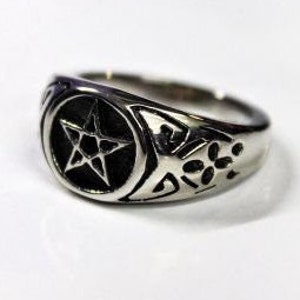 May include: A silver ring with a black pentagram design in the center. The ring has a textured band with a floral pattern.