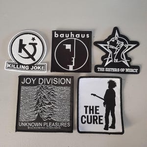 May include: Five black and white embroidered patches featuring the band names Bauhaus, Killing Joke, The Sisters of Mercy, Joy Division, and The Cure. The patches are all rectangular except for The Sisters of Mercy patch, which is a star shape.