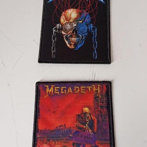 Puede incluir: Dos parches cuadrados negros con el nombre de la banda "MEGADETH". Uno presenta una calavera con cadenas, el otro una figura en un paisaje rojo. Ambos tienen bordes negros, para coser o planchar.