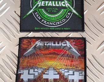 May include: Two Metallica band patches. The top patch is black with green and white graphics, including the band's name and "Since 1981." The bottom patch features the band's name and "Master of Puppets" with a sunset design.