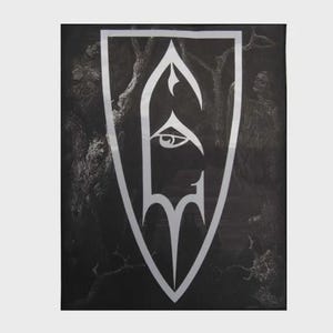 May include: A rectangular black fabric wall hanging featuring a large, white, shield-shaped emblem in the center. The emblem contains a stylized eye graphic. The background displays a dark, monochromatic forest scene with bare, gnarled tree branches.
