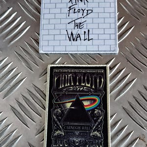 May include: Two Pink Floyd embroidered patches. One features the text "Pink Floyd The Wall" over a brick wall design. The second patch has the text "The Dark Side of the Moon Tour 1972" with a prism and rainbow.