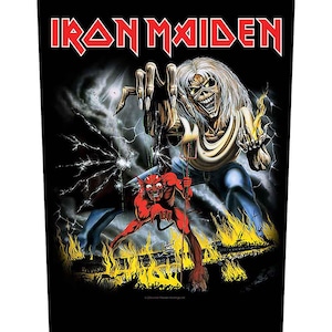 Peut inclure: Graphique noir avec le nom du groupe "Iron Maiden" en rouge. L'illustration montre une figure squelettique aux longs cheveux blancs, tendant la main. Un diable rouge est devant des flammes.