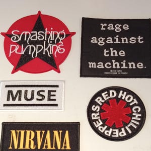 Puede incluir: Un conjunto de parches bordados con logotipos y textos de bandas. Incluye un parche rojo en forma de estrella con "Smashing Pumpkins", un cuadrado negro con "rage against the machine", un rectángulo blanco con "MUSE", un rectángulo negro con "NIRVANA" y un parche circular con "Red Hot Chili Peppers".