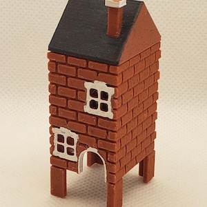 Pode incluir: Uma pequena casa de tijolo vermelho com telhado preto e janelas brancas. A casa tem uma chaminé e está elevada sobre quatro pernas.