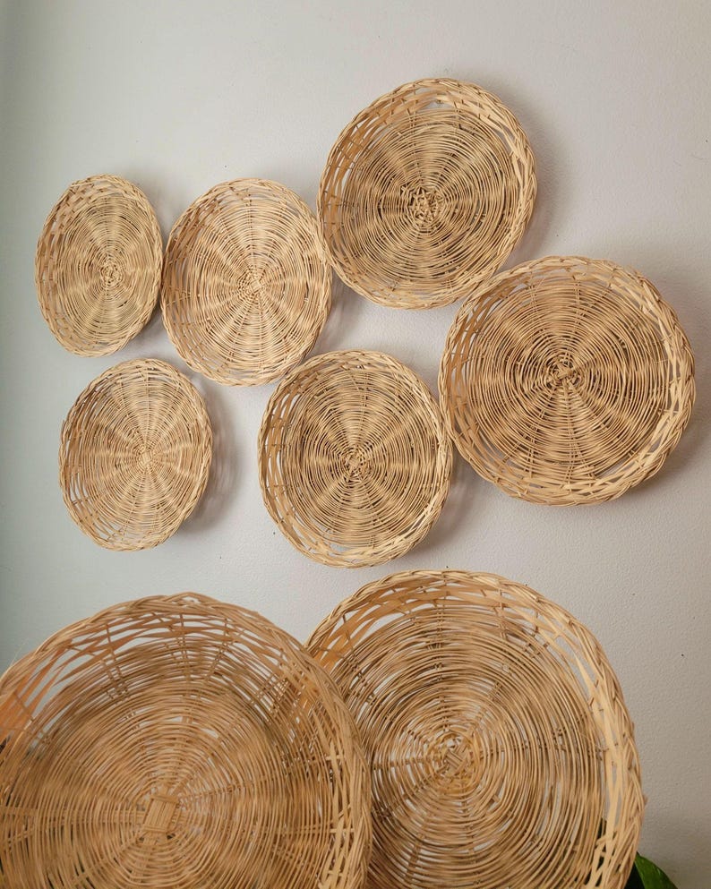 May include: A collection of eight round, light brown woven wicker baskets of varying sizes arranged in a cluster. Each basket features a circular, spiraling weave pattern made from thin, natural-colored reeds, creating a textured, open-work design.