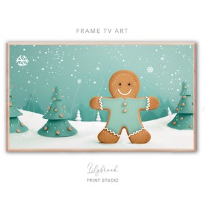 May include: A gingerbread man cookie in a blue and white winter scene with snow falling. The gingerbread man is wearing a blue shirt and has a white smile. There are three green trees in the background.