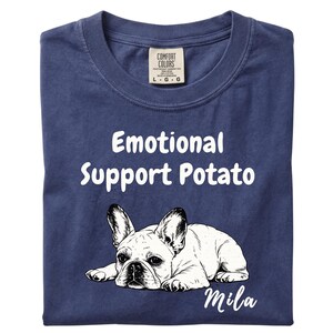 May include: A navy blue t-shirt featuring the white text "Emotional Support Potato" above a black and white line drawing of a French Bulldog lying down, with the name "Mila" written in white script below the dog and a Comfort Colors brand label.