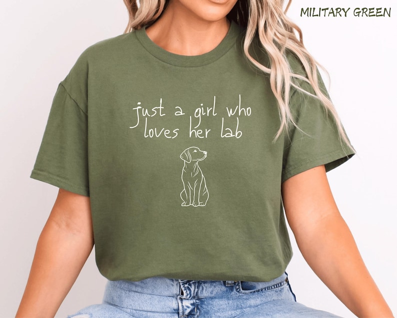 Puede incluir: Camiseta verde militar con el texto "just a girl who loves her lab" y un contorno blanco de un perro. La camiseta es de color liso y tiene mangas cortas.