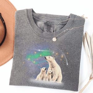 May include: Gray t-shirt with a graphic of three polar bears standing in front of a starry sky with a green aurora borealis. The shirt has the text "Comfort Colors" on the tag.