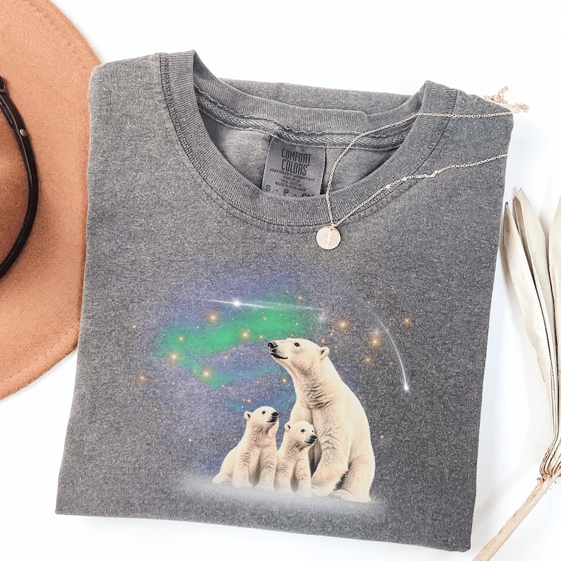 May include: Gray t-shirt with a graphic of three polar bears standing in front of a starry sky with a green aurora borealis. The shirt has the text "Comfort Colors" on the tag.