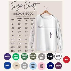 Puede incluir: Una sudadera unisex blanca Gildan 18000 cuelga de una percha de madera. La imagen incluye una tabla de tallas con medidas en pulgadas para el ancho, largo y largo de la manga, junto con muestras de color.
