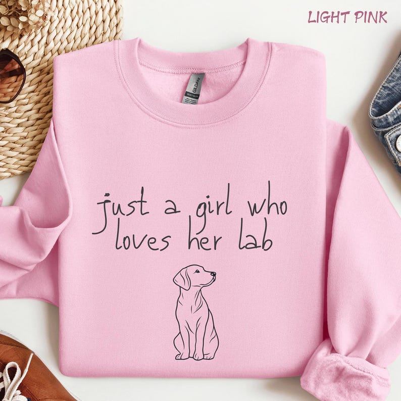 Puede incluir: Sudadera rosa claro con la frase "just a girl who loves her lab" en escritura negra. Un dibujo lineal negro de un Labrador Retriever est&aacute; debajo del texto. Las palabras "LIGHT PINK" est&aacute;n en la parte superior.