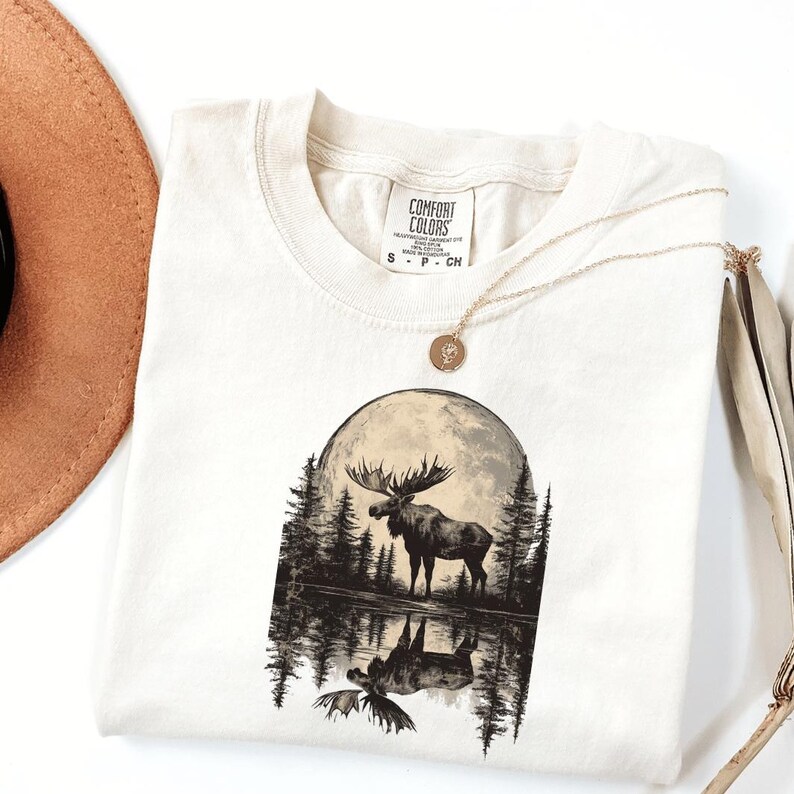 May include: A white t-shirt with a black and white graphic of a moose standing in a lake with a full moon behind it. The text "COMFORT COLORS" is on the tag.